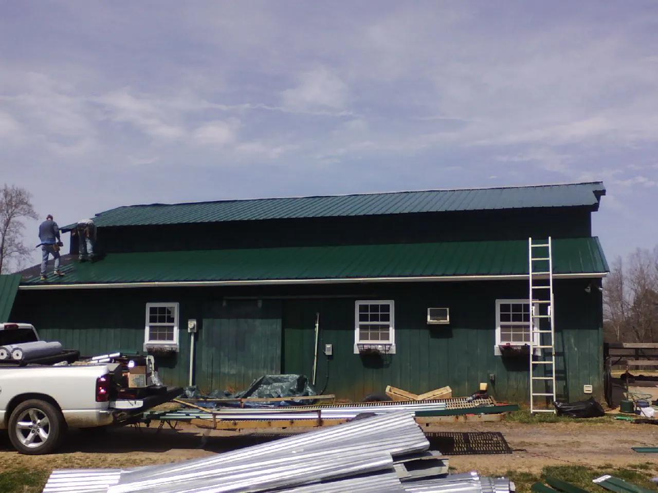 Crew installing green metal roofing on a large green barn in Greenwood